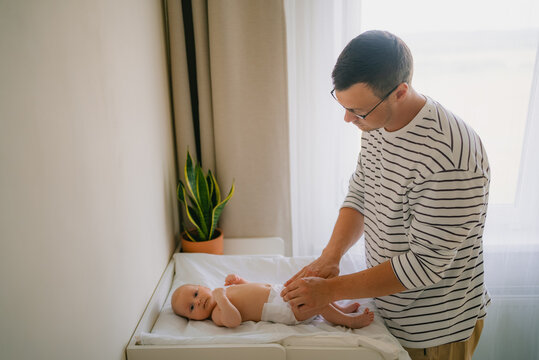 Father performing a diaper change for his newborn baby, demonstrating modern fatherhood and nurturing care during a daily routine on a changing table in a brightly lit room