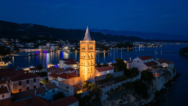 Aerial view of Old Town Rab with its illuminated bell tower and historic stone buildings overlooking the harbor at night in Rab, Primorsko-goranska zupanija, Croatia.