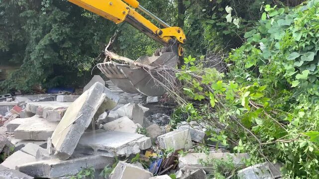 Yellow excavator bucket lifts heavy concrete debris and rubble in an outdoor demolition area, site clearance, urban redevelopment, land preparation.