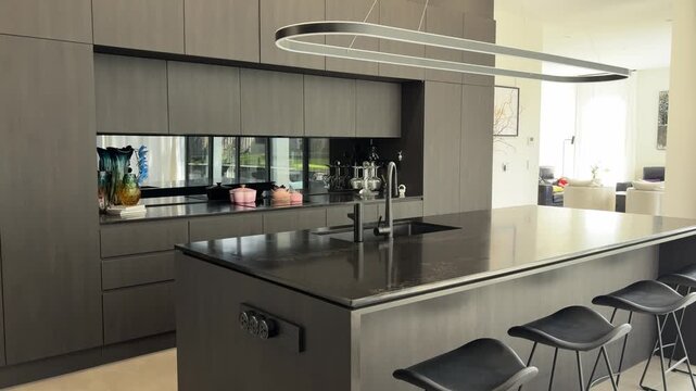 Slow lateral view of modern open plan kitchen with large island and floor-to-ceiling windows
