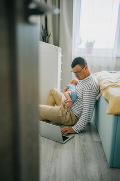 Father balancing parental duties with professional responsibilities, holding a baby on his chest while focused on a laptop, embodying the demands of working from home with a newborn