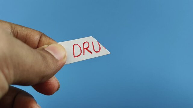 Closeup of addict person hand holding white paper with drugs word text written on it cut using scissor. Stop illegal drug addiction habit awareness concept.