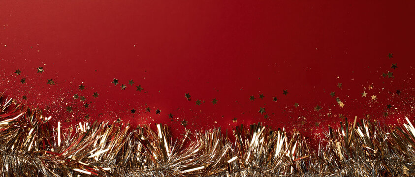 Bold holiday celebration background ideal for Christmas and New Year campaigns. Gold tinsel garland and scattered star confetti pop against deep crimson red, with generous copy space above.