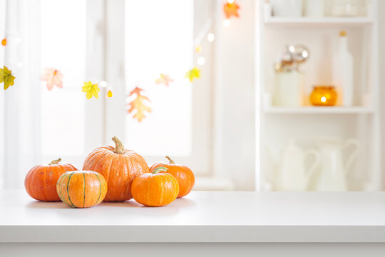 Ripe autumn pumpkins on white table top with design space and blurred decorated for holiday interior background
