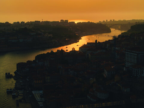 Aerial view of the Douro River winding through historic Porto at sunset, with golden light reflecting on the water and traditional rooftops in Porto, Porto District, Portugal.