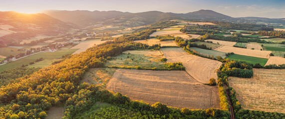 Naklejka premium Aerial drone panorama of patchwork farmland and rolling hills at golden hour sunset.