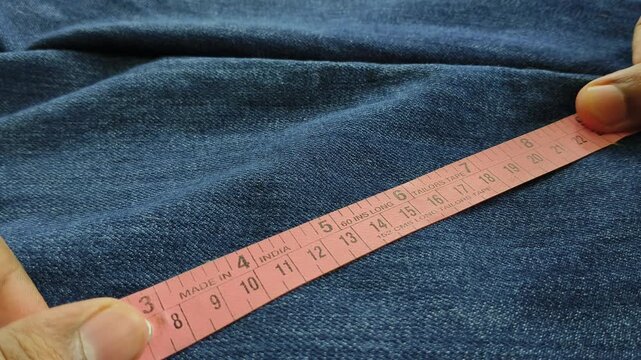Tailor hand measure size of old used denim jeans fabric or cloth using measuring tape to do damage restoration repair and maintenance for sustainable reuse. Clothes recycle to reduce waste concept.