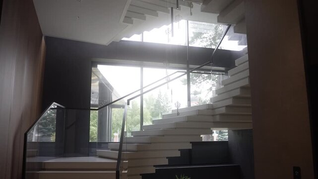 Modern floating staircase in bright atrium with backlit windows and glass balustrade, low mid-level upward viewpoint emphasizing diagonal geometry and minimalist mood