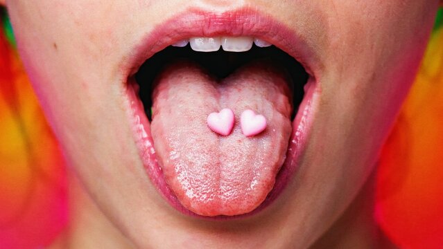 Close up of a person with two small pink heart candies resting on their tongue