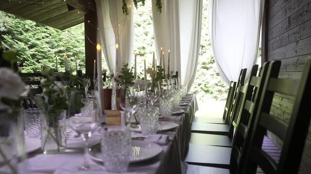 Rustic porch dining table with lit candles and crystal glassware under sheer curtains, with dining, table, candle, glassware detail, showing crystal, plate, napkin cutlery context