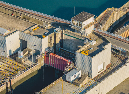 Aerial view of hydroelectric dam machinery, water control gates, and industrial structures regulating the Rhone river flow in Saulce-sur-Rhone, Auvergne-Rhone-Alpes, France.