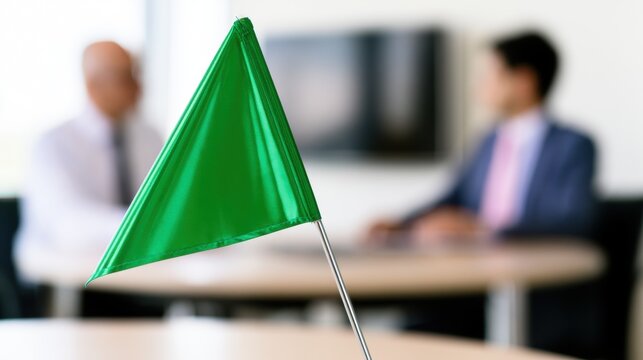 Green flag in focus with two people in the background during a meeting in a modern office setting