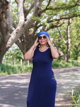 Elegant Mature Woman in Blue Dress and Sunglasses Posing in a Green Park