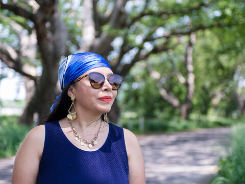 Elegant Mature Woman in Blue Dress and Sunglasses in a Green Park