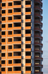 Unfinished red brick high rise residential building under construction with empty window openings and balconies. © zhennyzhenny