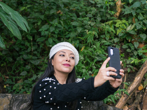 Woman Taking a Selfie While Sitting on a Bench in a Natural Park