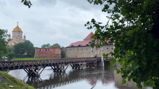 Historical Fagaras Citadel with its wooden drawbridge over the moat and an orthodox cathedral in the background on a cloudy summer day