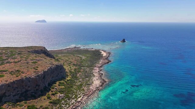 Limestone cliffs and rocky shoreline extend along the Gramvousa Peninsula near Balos, Kissamos, Chania, Crete, Greece, with offshore rock formations during a drone forward flyover.