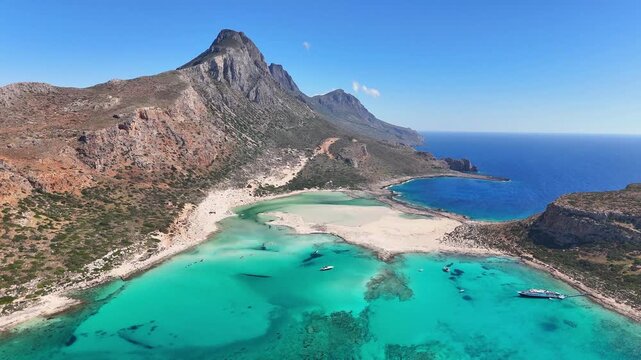 Balos Lagoon shows turquoise shallows, white sandbars, Gramvousa Peninsula and Platiskinos mountains on the coast of Crete, drone forward flyover.