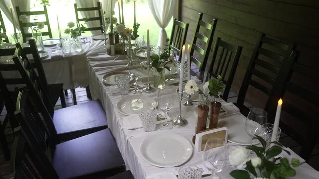 Long rustic dining table set with lit taper candles and floral centerpieces in softly lit room, with dining, table, formal, setting detail, showing candle, candlestick, candlelight, 