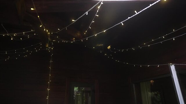Warm string lights suspended beneath dark wooden ceiling with exposed beams creating cozy overhead glow, with light, string, led, bulb detail, showing warm, glow, yellow,
