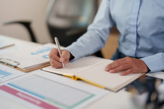 Cropped businesswoman writing notes in notebook at office desk for financial strategy and data analysis