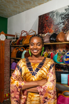 African woman small business owner smiling with arms crossed in her handbag store, SME