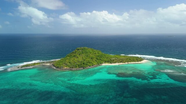 Aerial orbit circles small green islet fringed with white sand and coral reef in turquoise Caribbean waters near Sandy Island Grenada