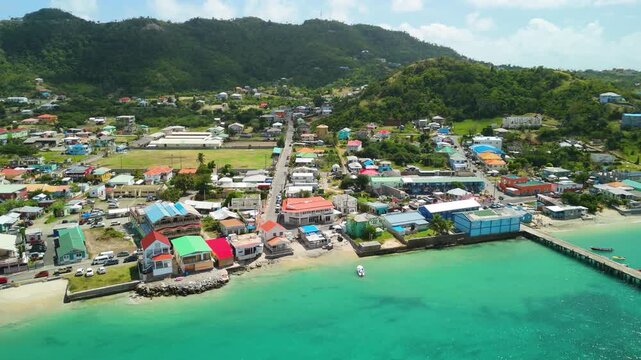 Coastal town Hillsborough Carriacou Grenada spreads along turquoise bay with jetty, colorful rooftops and green hills behind