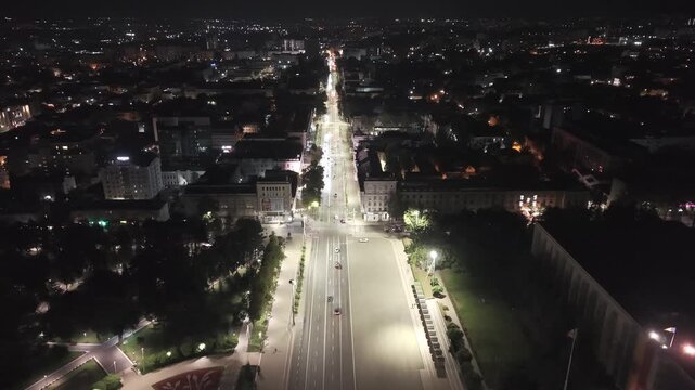 Night aerial pullback over central Chisinau, Moldova, revealing Stefan cel Mare Boulevard, Great National Assembly Square, the Triumphal Arch, city lights, traffic and surrounding downtown architectur