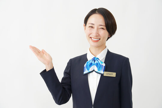 左側を手のひらで指すミドル女性スタッフ　白背景