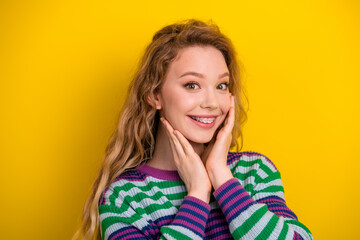 Fototapeta premium Young female student smiles in a colorful striped jumper against a bright yellow background