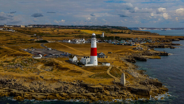 Aerial view of Portland Bill Lighthouse on the rocky coastline of the Isle of Portland with grassy fields and the English Channel in Portland, Dorset, United Kingdom.