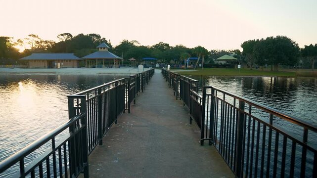 Golden hour view down the fishing pier at Waterfront Park in Clermont, Florida, leading to lakeside pavilions, palm trees, and the calm waters of Lake Minneola.