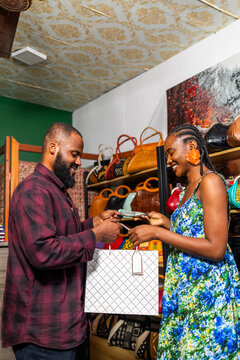 African female entrepreneur selling a handbag to a male customer in her store
