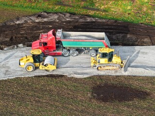 road roller, bulldozer and dump truck are processing gravel for a new road through previously undeveloped rural land  construction site from a bird's-eye view  road construction  infrastructure © keBu.Medien
