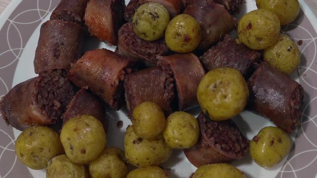 Cooked morcilla slices and seasoned baby potatoes sit on a plate beside a bowl of chopped aji dipping sauce on a wooden table.