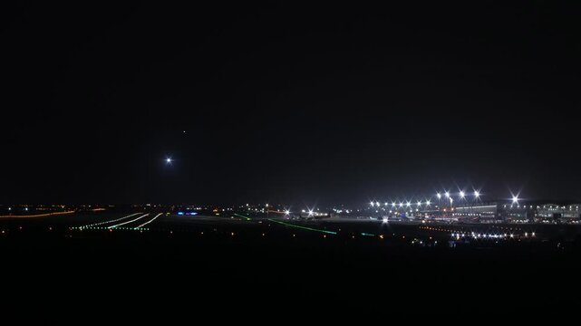 Cinematic night timelapse of an active airport runway featuring airplanes landing and airport fire trucks performing safety checks on the tarmac. Alicante airport, Spain.