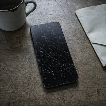 Cracked phone screen lying dark on a bare kitchen table