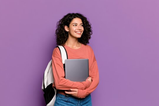 Young female student with curly hair smiling and holding a laptop against a purple background
