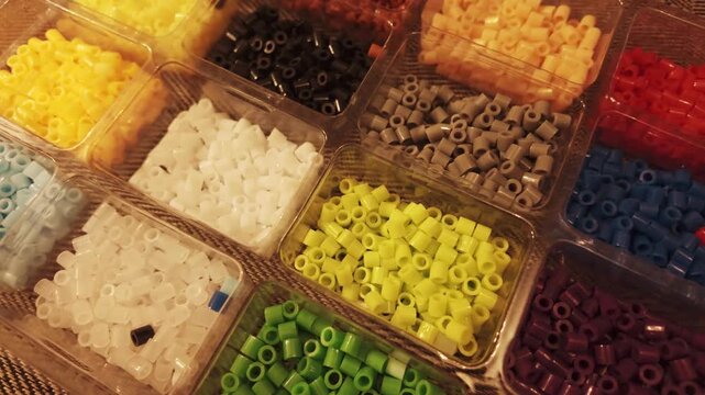 Top view of multicolored plastic perler beads organized in a partitioned storage container for arts and crafts projects.