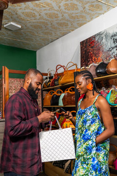 African female small business owner receiving mobile payment from a male customer in her handbag boutique