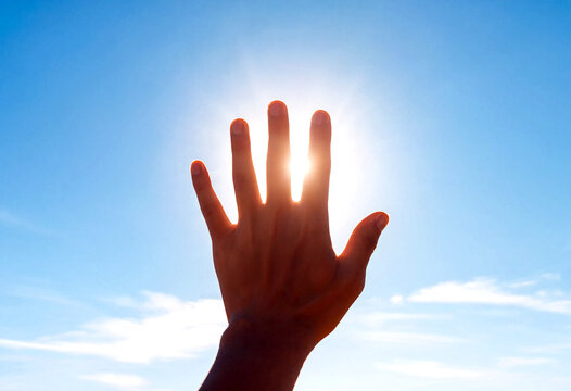 Silhouette of a hand reaching out towards the bright sun in clear blue sky