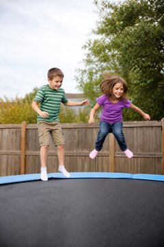 Kids joyfully jumping on trampoline near wooden fence