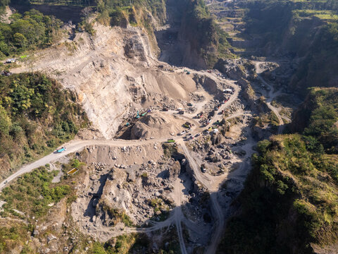 Aerial view of a large stone quarry with heavy machinery, trucks, and dirt roads winding through the rocky landscape in Klaten, Central Java, Indonesia.