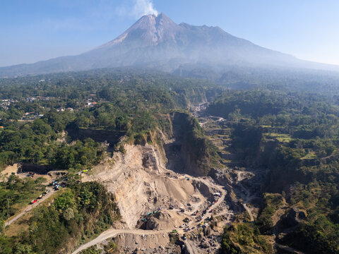 Aerial view of Mount Merapi volcano with mining operations in the foreground, surrounded by lush tropical vegetation in Klaten, Central Java, Indonesia.