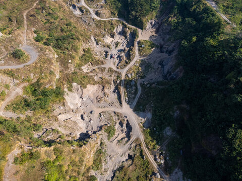 Aerial view of a quarry with dirt paths winding through rocky terrain and surrounding lush green vegetation in Klaten, Central Java, Indonesia.
