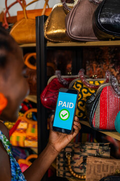 African woman small business owner successfully completing a mobile momey payment transaction for bags in her boutique