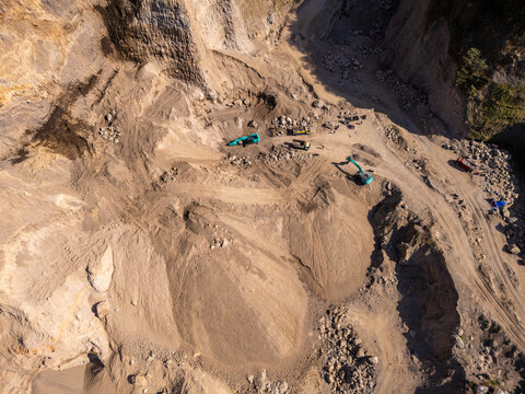 Aerial view of a sand quarry with excavators working on piles of sand and rocky terrain in Klaten, Central Java, Indonesia.