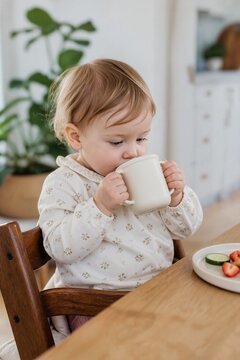 Toddler enjoying a drink while sitting at a wooden table